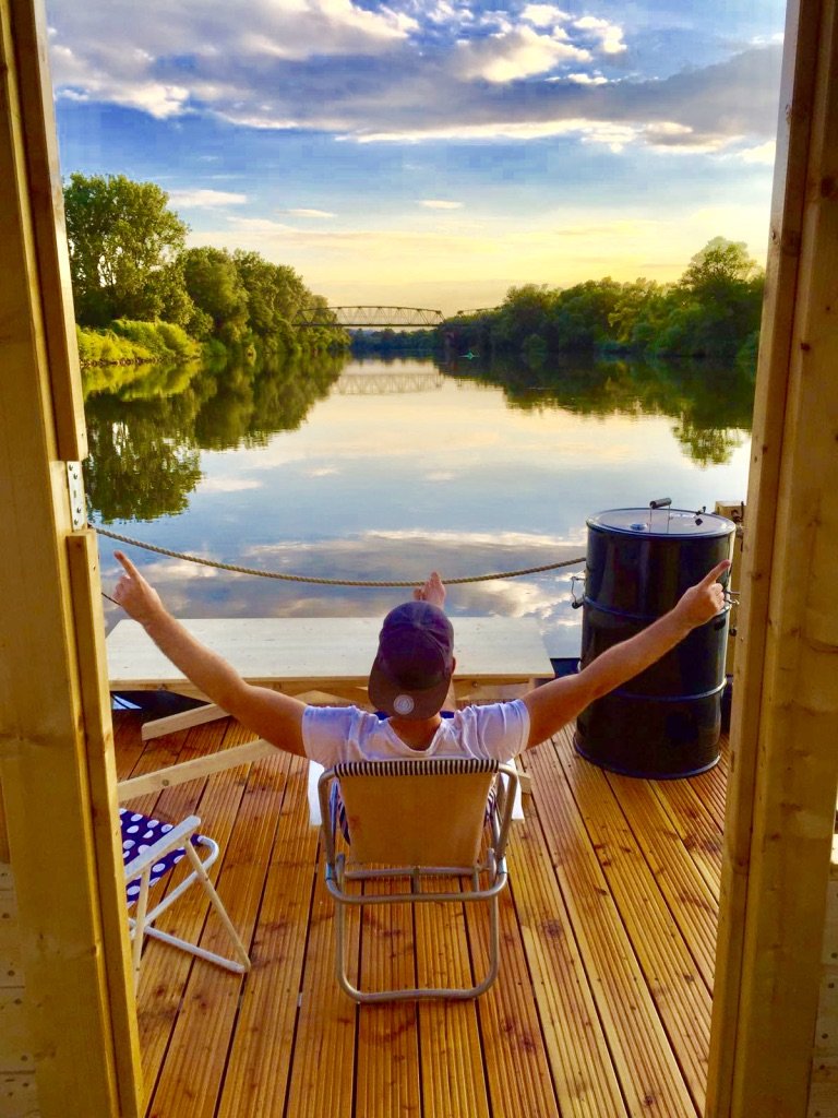 Moritz Gräbner, von hinten, auf dem Deck seines Floßes auf dem Main bei Abendlicht, die Arme ausgebreitet